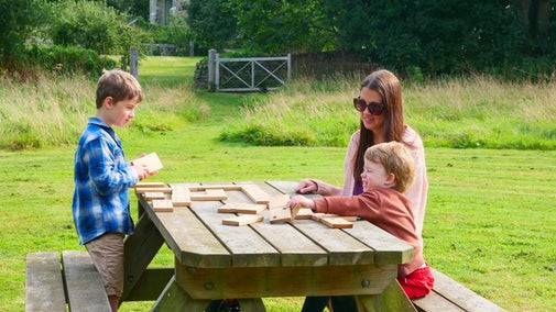A family sits at a bench and plays a game of dominoes outside